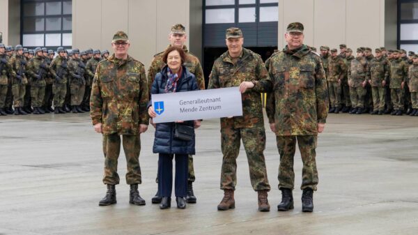 Generalleutnant Ingo Gerhartz (2. v. r.) und Karin Mende, die Ehefrau des verstorbenen Namenspatrons, übergeben bei einem feierlichen Appell das neue Gebäudeschild an die Führungskräfte der bodengebundenen Luftverteidigung auf dem Platz vor dem Neubau des Ausbildungszentrums Flugabwehrraketen.