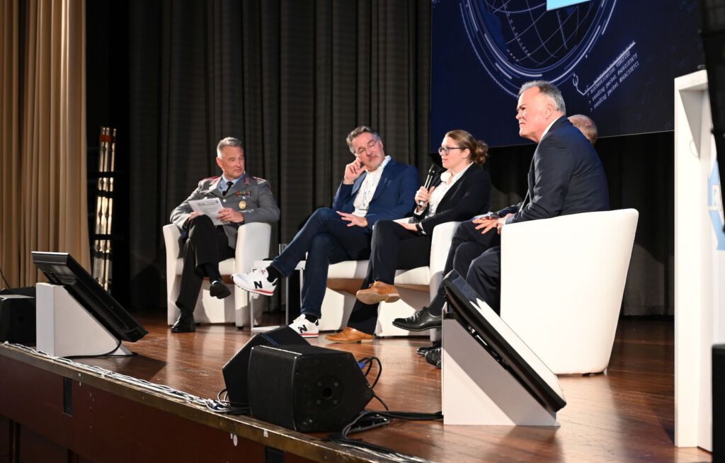 Sabine Kammerhofer von der Unternehmensberatung CGI Deutschland spricht bei einer Podiumsdiskussion. Auch im Bild: Oberst i. G. Dr. Joachim Bartels (Moderation), Dr. Willfried Wienholt von IABG, Ramon Mörl von itWatch (v. l. n. r.)