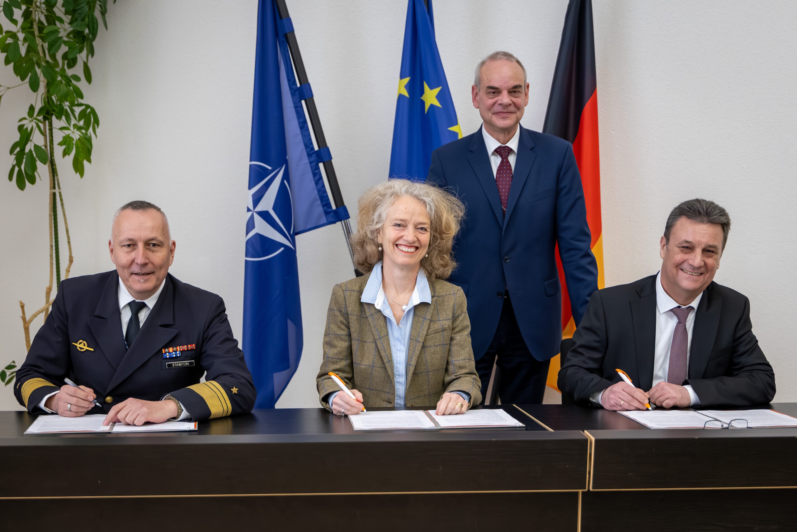 Rüstungsbeschaffung der Zukunft: Staatssekretär Zimmer (stehend), Vizeadmiral Stawitzki (l.), Prof. Kern (m.) und Vizepräsident des BAAINBw Herzog (r.) bei der Unterzeichnung